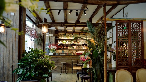 Un café acogedor con vigas de madera, plantas colgantes y diversas opciones de asientos.