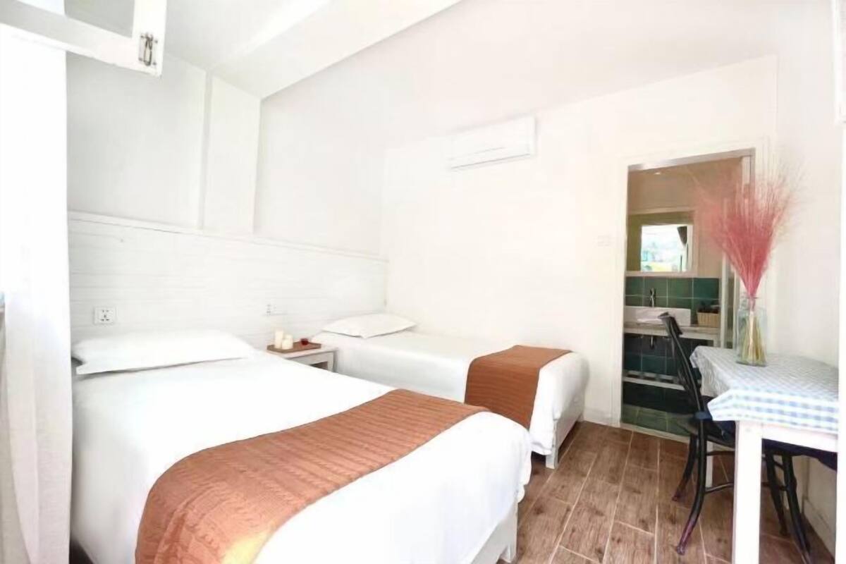 Habitación de hotel con dos camas, una mesita con una silla y una zona de kitchenette.