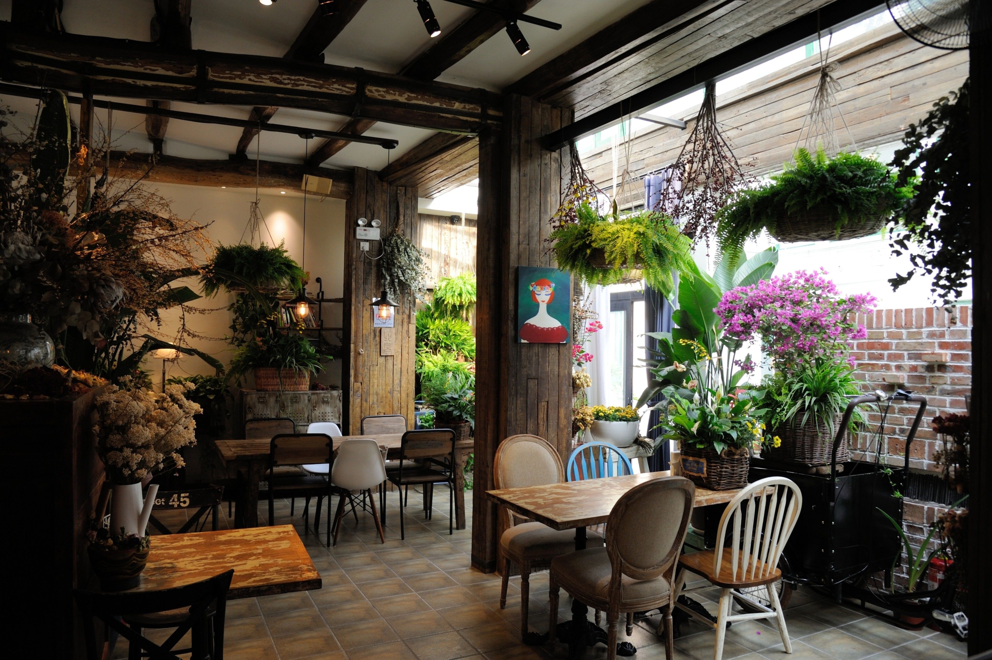 Un café acogedor con mesas y sillas de madera, plantas colgantes y una decoración rústica.