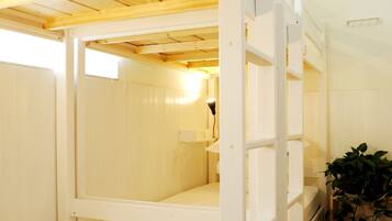Habitación con literas, techo de madera, paredes blancas y una planta en maceta.