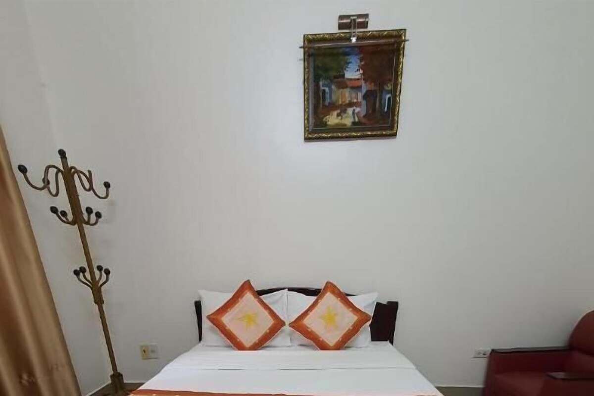 Habitación de hotel con una cama grande, un perchero, un cuadro en la pared y una silla roja.