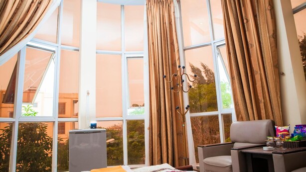 A room with a large window, a bed with a quilt, a chair, a small table with snacks, and a decorative wall hanging. - Star Hotel Hai Duong (Hai Phong)