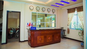 A reception area with a wooden counter, clocks, and a window with curtains. - Star Hotel Hai Duong (Hai Phong)