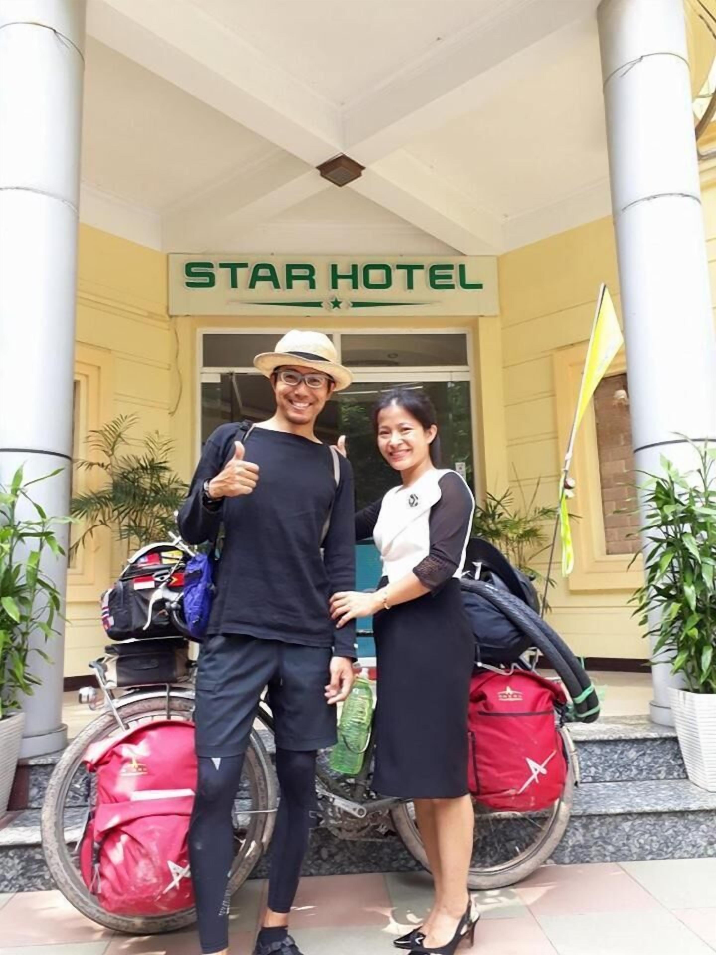 Un hombre y una mujer de pie frente a la entrada del Hotel Star, con una motocicleta y equipaje cerca.