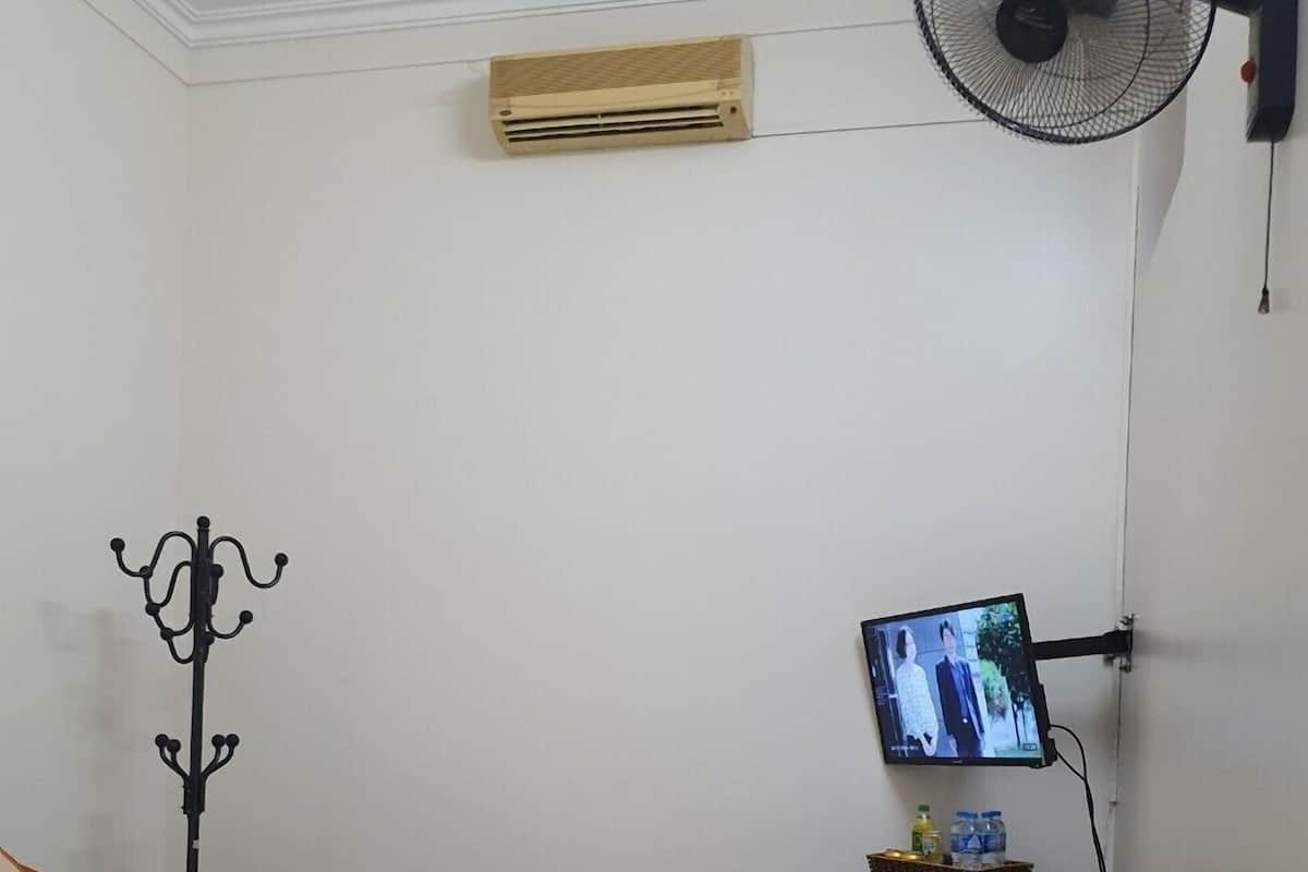 A bedroom with a bed, a wall-mounted TV, a standing fan, and a coat rack.