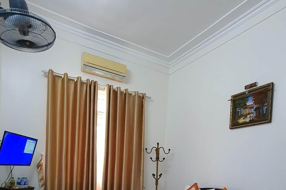A hotel room with a bed, a desk with a computer, a coat rack, and a painting on the wall.