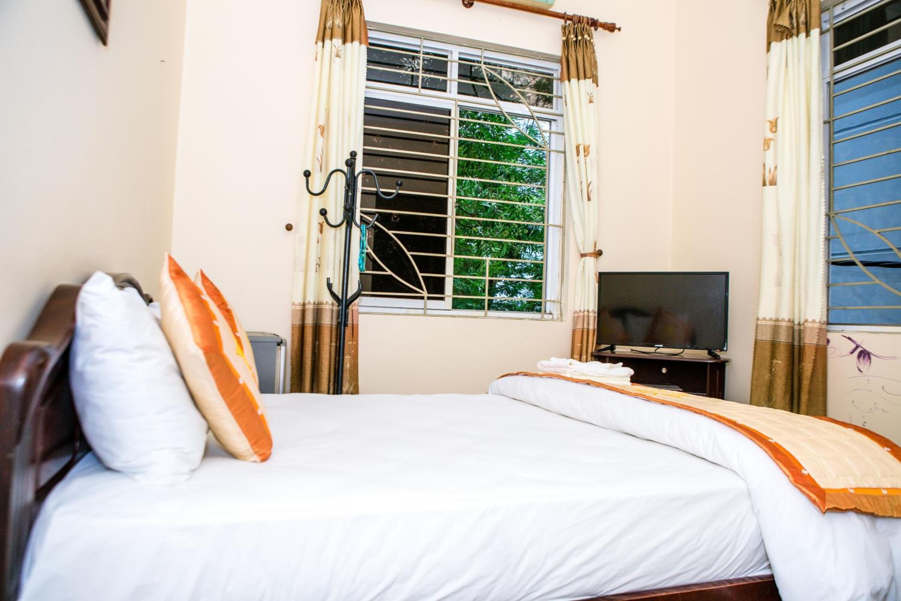 Une chambre à coucher avec un lit, une télévision et une fenêtre avec des rideaux.