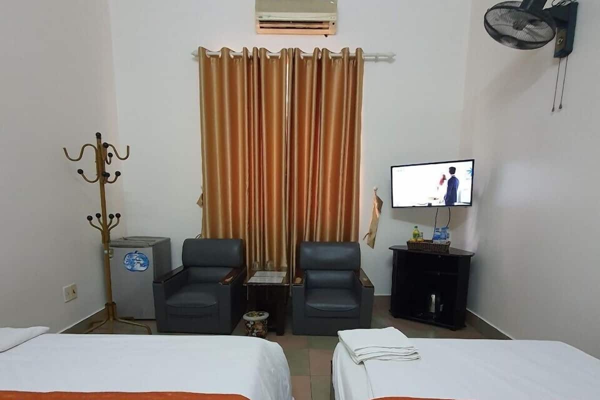 A hotel room with two beds, a television, a small table, a chair, a coat rack, and an air conditioning unit.