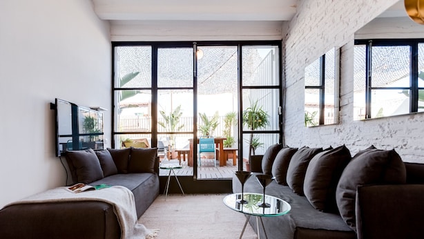 Una sala de estar moderna con un sofá seccional, una mesa de centro de vidrio y ventanas amplias que ofrecen vistas del exterior.