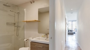 Un baño moderno con ducha de vidrio, lavamanos blanco y tocador de madera.
