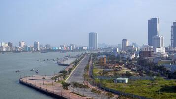 A waterfront cityscape with a prominent road running parallel to the water, lined with palm trees and a pedestrian walkway.