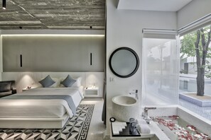 A modern hotel room with a large bed, bedside tables, a round mirror, a sink, and a view of the outside.