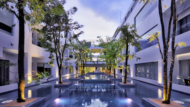 A modern indoor pool area with a central water feature, surrounded by trees and modern architecture. - Chan Boutique (Sihanoukville)