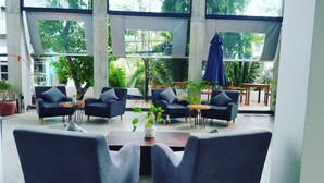 A modern indoor seating area with multiple sofas and tables, large windows with a view of greenery, and a concrete structure. - Chan Boutique (Sihanoukville)