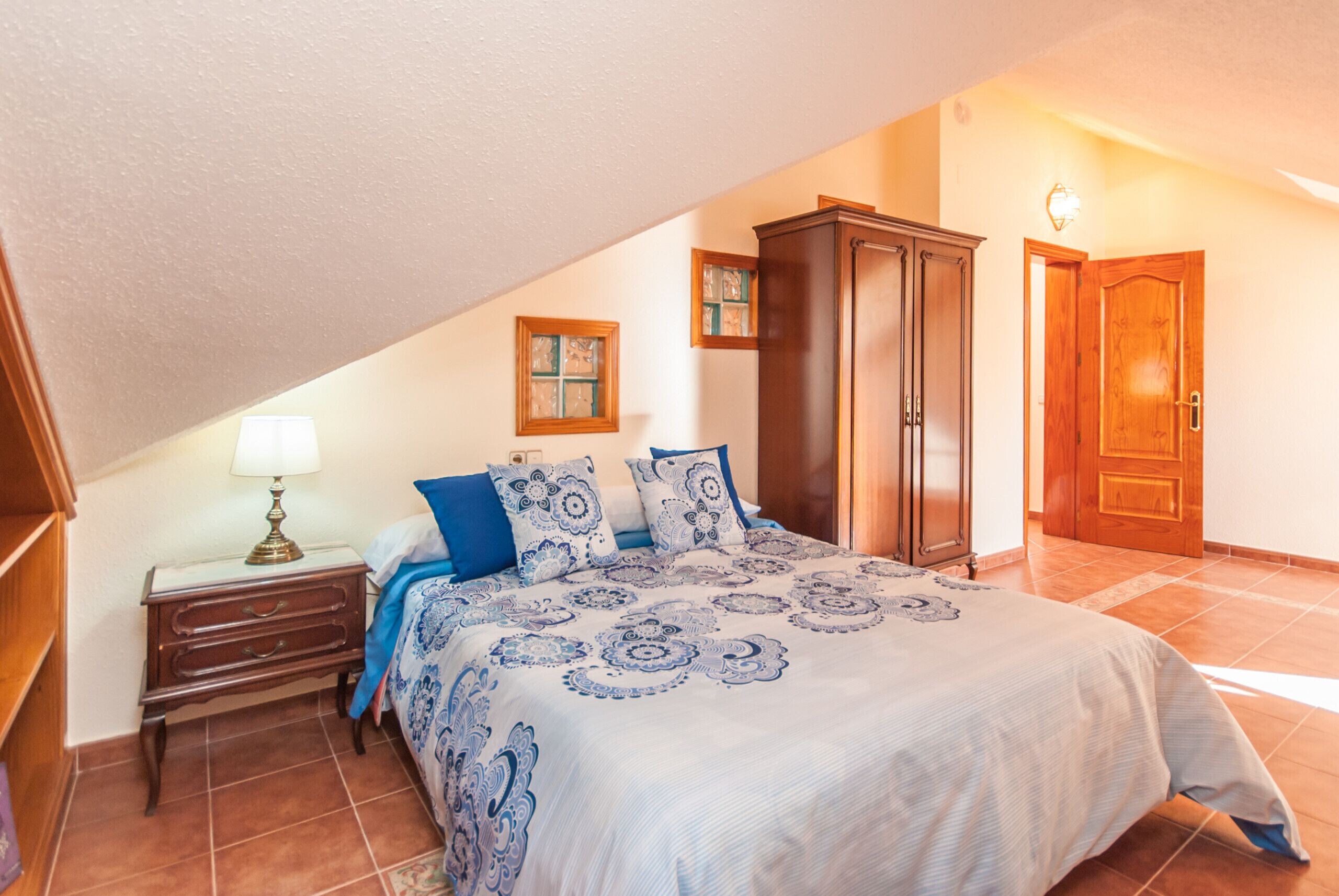 A bedroom with a bed, a nightstand, a wardrobe, and a door.