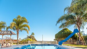 Ein klares, blaues Schwimmbecken mit einer blauen Rutsche, umgeben von Palmen und einem Pavillon.