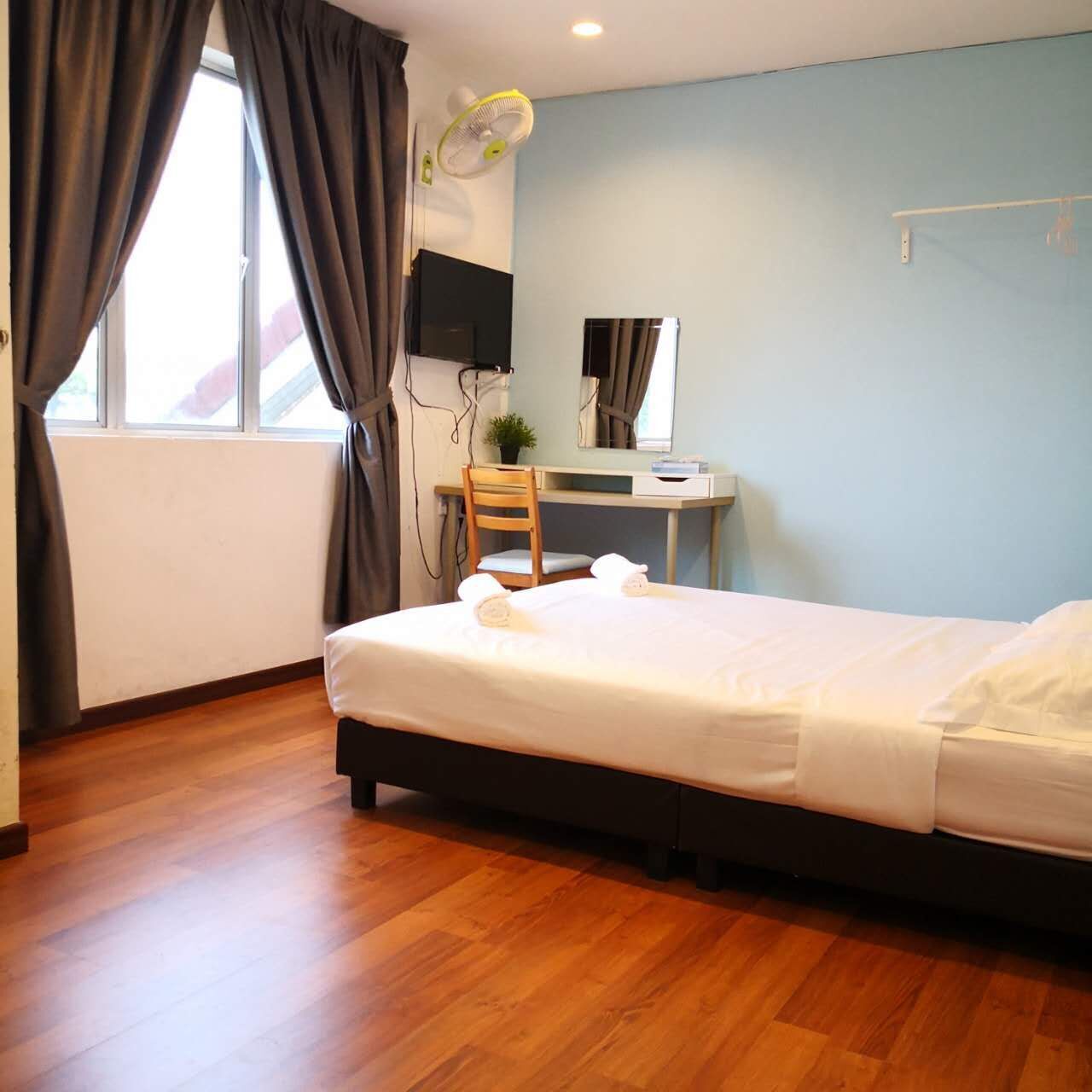 A bedroom with a bed, a desk, a chair, a TV, and a fan.
