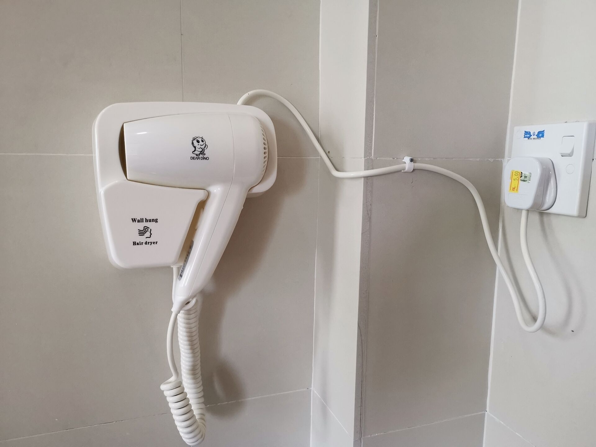 Een aan de muur bevestigde haardroger met snoer, aangesloten op een stopcontact.
