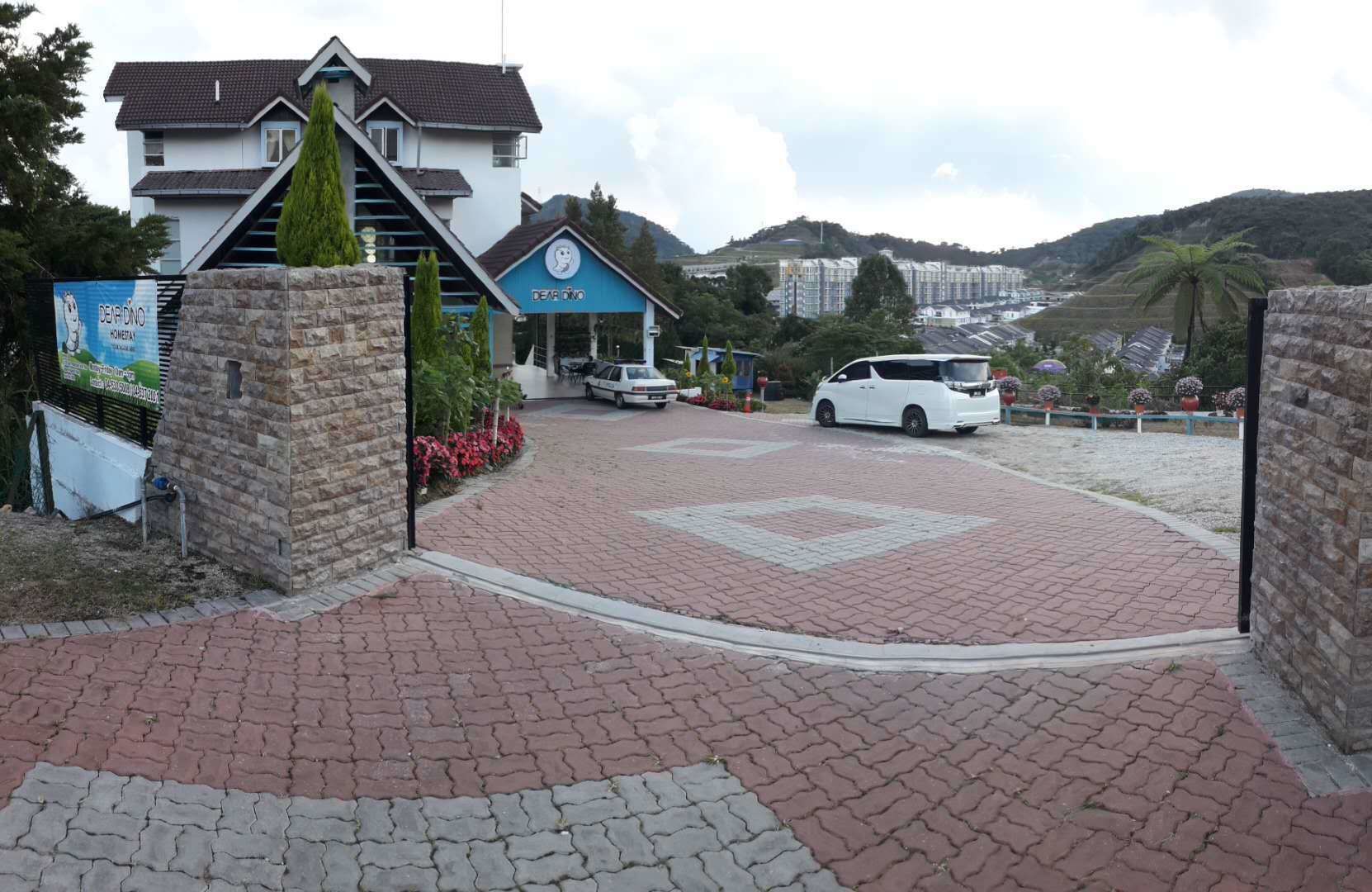 A hotel entrance with a paved driveway, a blue building with a sign, and a white car parked nearby.