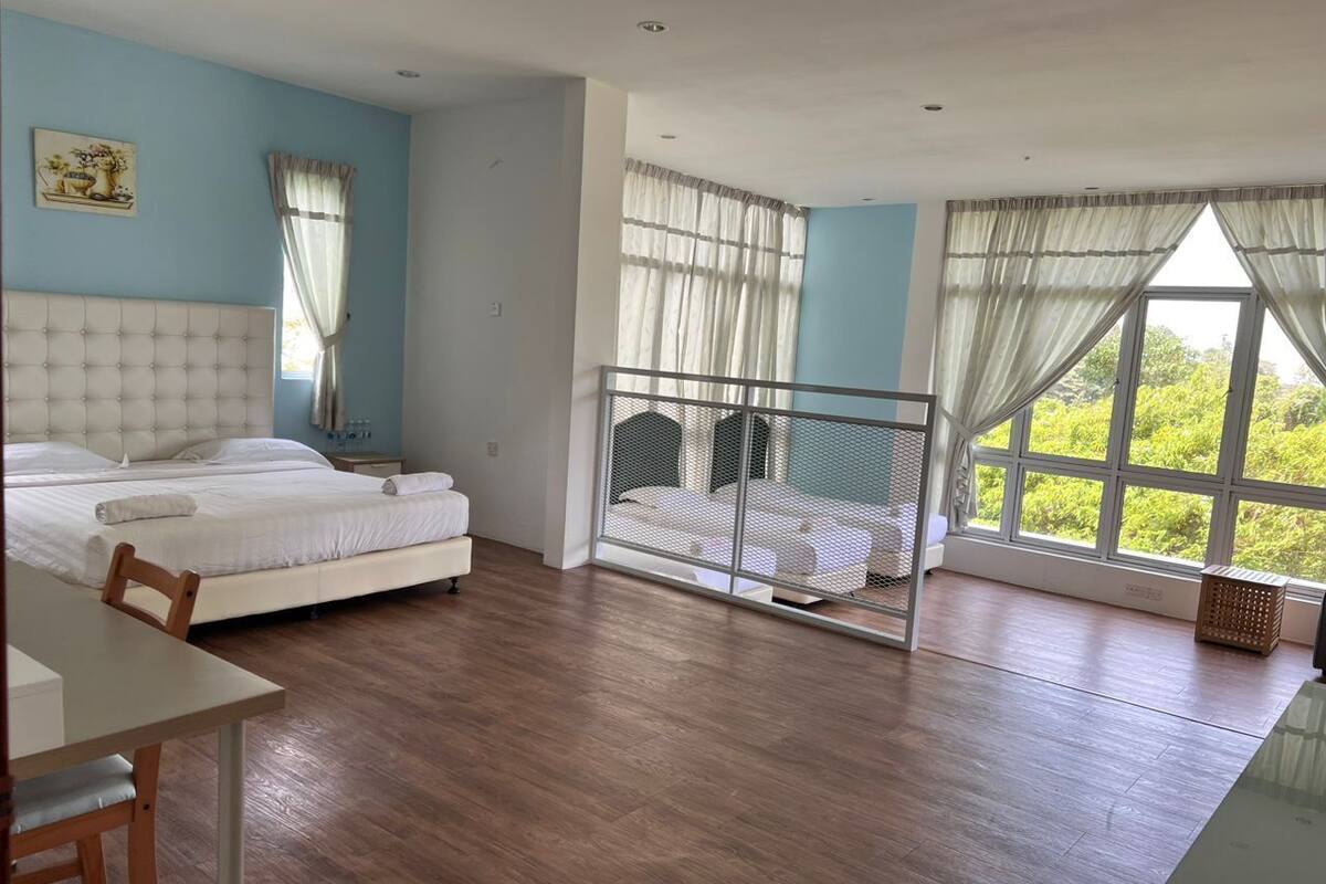 A bedroom with a bed, a desk, and a balcony with a view of greenery.