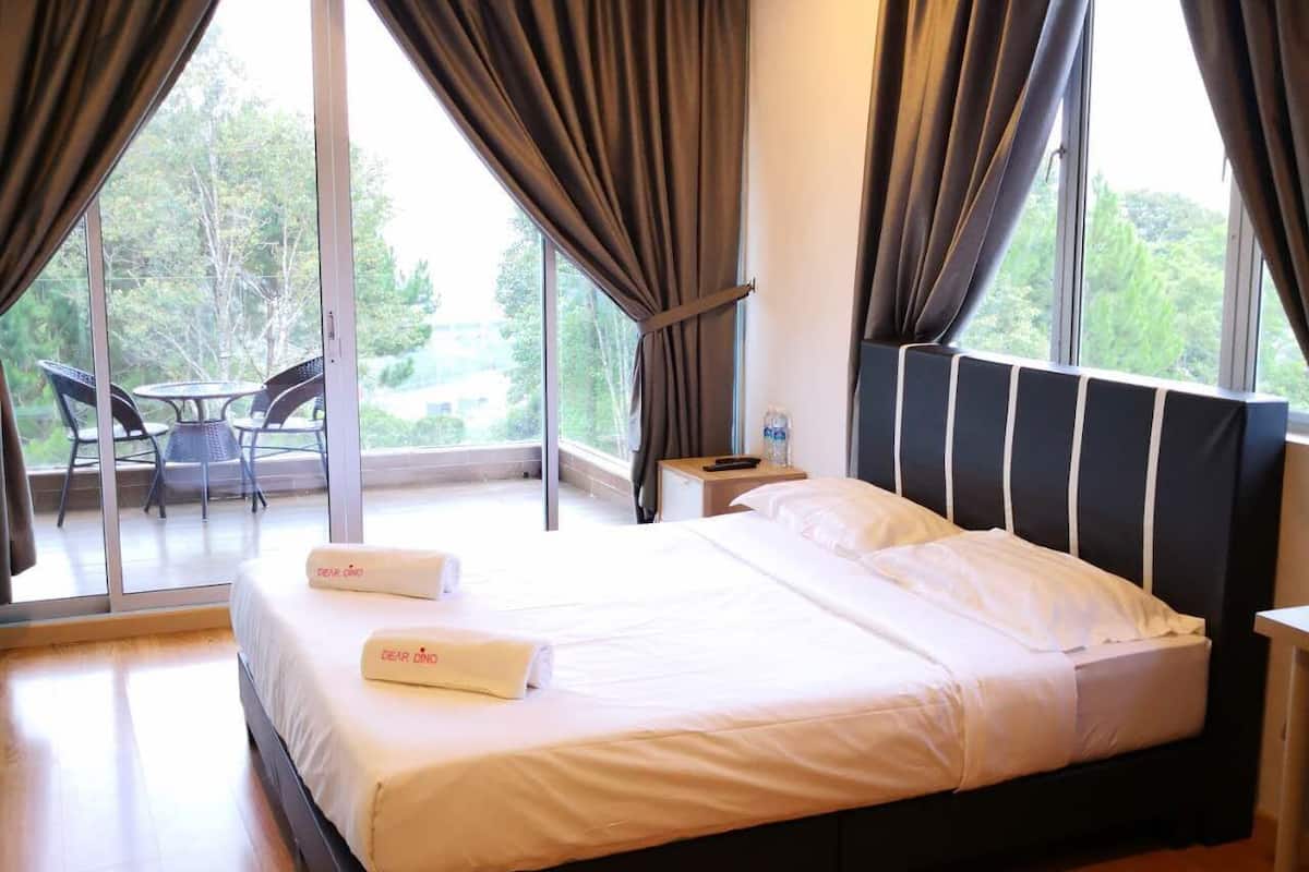 A hotel room with a large bed, a small table, and a chair near a sliding glass door leading to an outdoor area.
