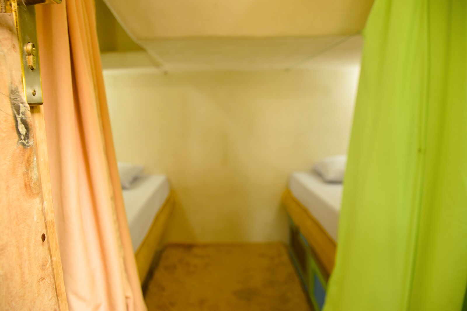 Een kleine, afgesloten badkamer met twee bedden, een houten deur en een groen gordijn.