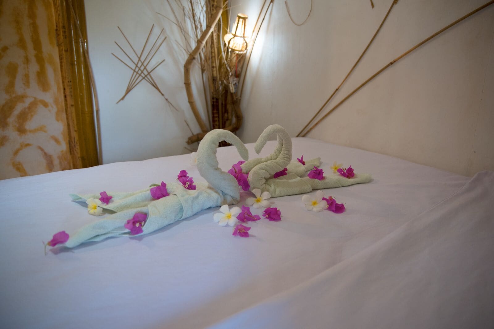 A bed with a towel arranged in the shape of a swan, adorned with pink and white flowers.