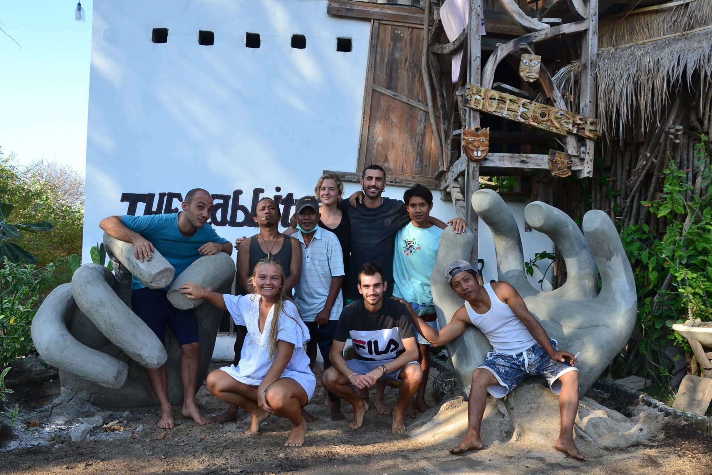A group of people posing in front of a large white wall with the text "TUCALBIT" and a wooden structure with carved figures.