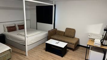 Una habitación con cama con dosel, un sofá, una mesita y un refrigerador.