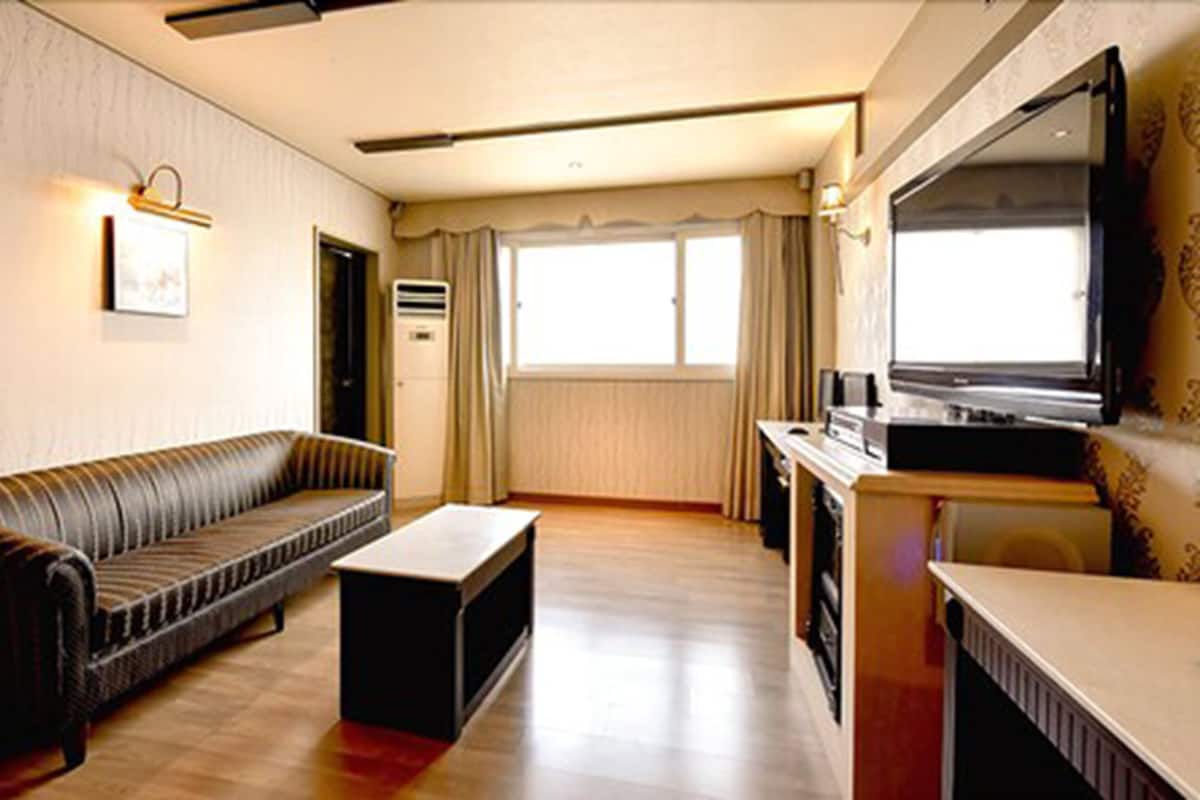 A living room with a sofa, a coffee table, a flat-screen TV, and a window with curtains.