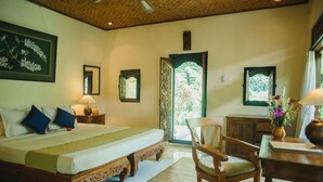 A bedroom with a bed, bedside table, chair, and a desk with a vase of flowers. - Alam Indah (Ubud)