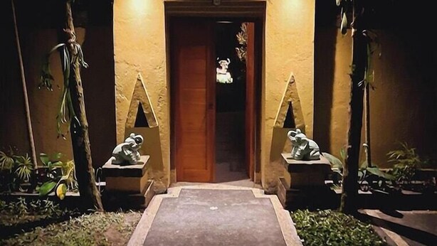 A well-lit entrance with a decorative pathway leading to a door, flanked by two statues and surrounded by greenery. - Alam Indah (Ubud)