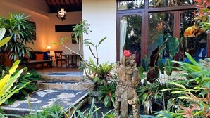 A tropical garden with a stone statue, a wooden bench, and a dining area with a table and chairs. - Alam Indah (Ubud)