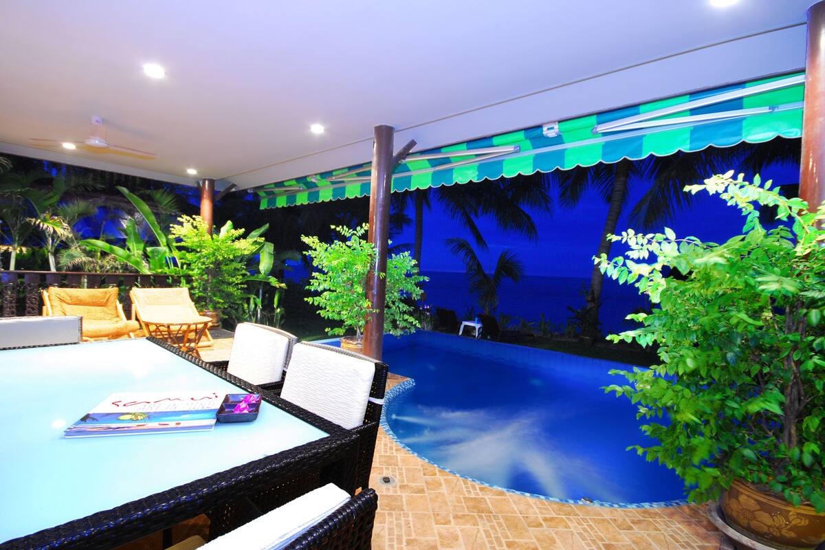 A room with a pool, lounge chairs, and tropical plants.