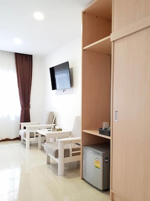 A hotel room with a TV mounted on the wall, a seating area with two chairs, a small refrigerator, and a wooden wardrobe. - D.I Residence Boutique Hotel (Phnom Penh)