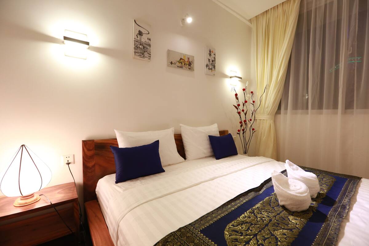Une chambre d’hôtel avec un lit bien fait, une table de chevet avec une lampe et des œuvres d’art accrochées au mur.