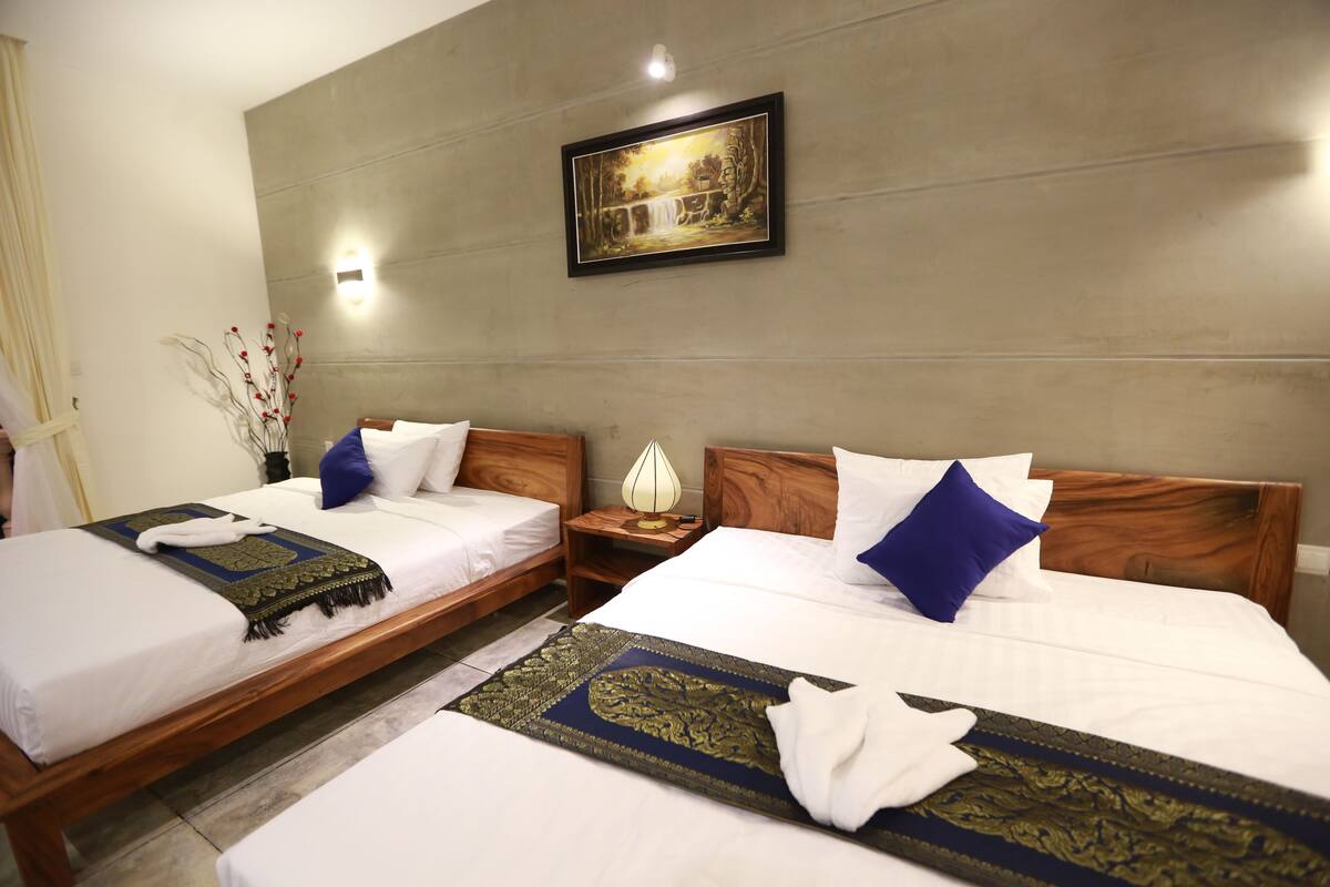 Une chambre d’hôtel avec deux lits, chacun étant équipé de draps blancs et d’oreillers bleus. Un tableau encadré est accroché au mur, au-dessus des lits.