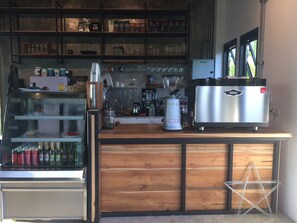 Une cuisine équipée d’une machine à café, d’étagères remplies de grains de café et d’un réfrigérateur.