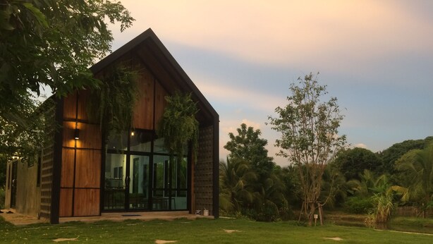 A modern building with large glass windows and a wooden facade, surrounded by a well-maintained lawn and tropical vegetation.