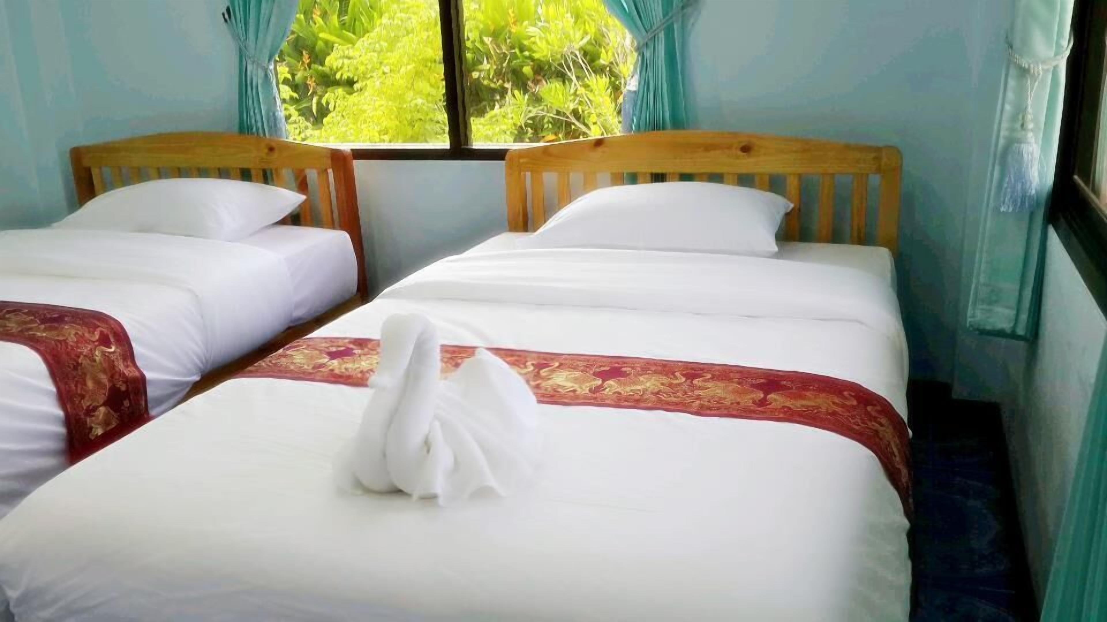Una habitación con dos camas individuales, cada una con ropa blanca y un detalle decorativo rojo.