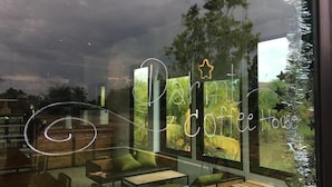 A cafe interior with a large window displaying a tropical view, a sign reading "Dari Coffee House," and a reflection of the sky.