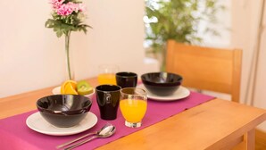 A breakfast table with a pink placemat, two black bowls, a glass of orange juice, and a flower vase.
