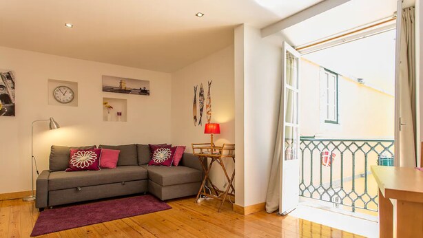 A living room with a grey sofa, red and white cushions, a wooden floor, a red lamp, and a small table.