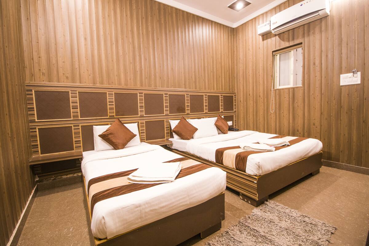 A hotel room with two beds, wooden paneling, a window, and an air conditioning unit.