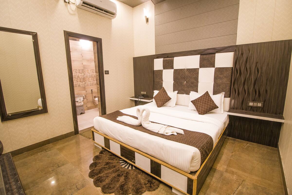 A hotel room with a large bed, a wooden headboard, a mirror, and a bathroom visible through an open door.