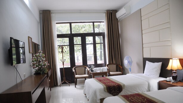 A hotel room with two beds, a desk, a chair, a TV, and a window with curtains.