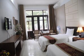 Habitación de hotel con dos camas, un escritorio, una silla, un televisor y una ventana con cortinas.