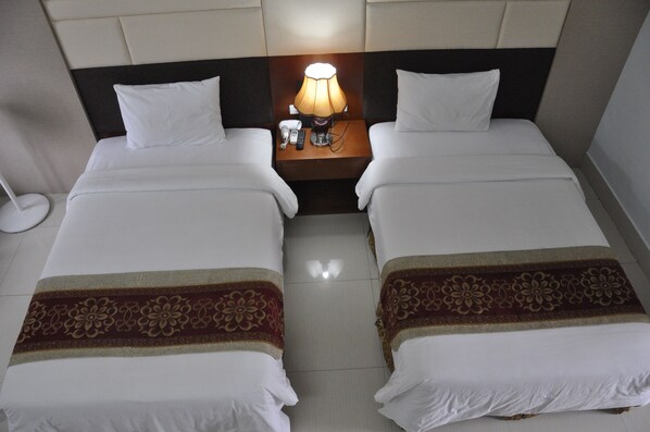 Una habitación de hotel con dos camas individuales, una mesita de noche con lámpara y un teléfono.