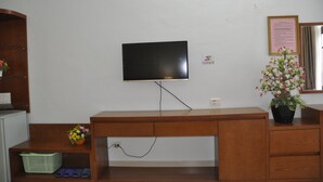 A room with a wooden desk, a television mounted on the wall, a small basket with a flower, and a potted plant.