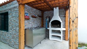 An outdoor kitchen area with a stone wall, a wooden pergola, and a pizza oven.